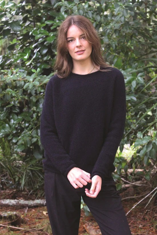 Black women's possum and merino wool crew neck jumper on female model standing in park. Lothlorian warm, soft, lightweight possum and merino wool womens pullover sweater