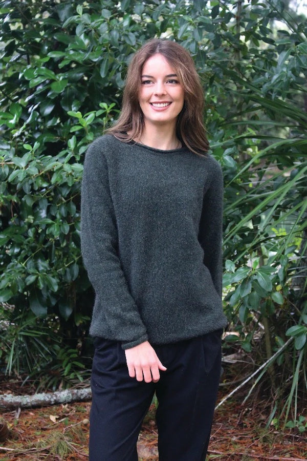 Green women's possum and merino wool crew neck jumper on female model standing in park. Lothlorian warm, soft, lightweight possum and merino wool womens pullover sweater