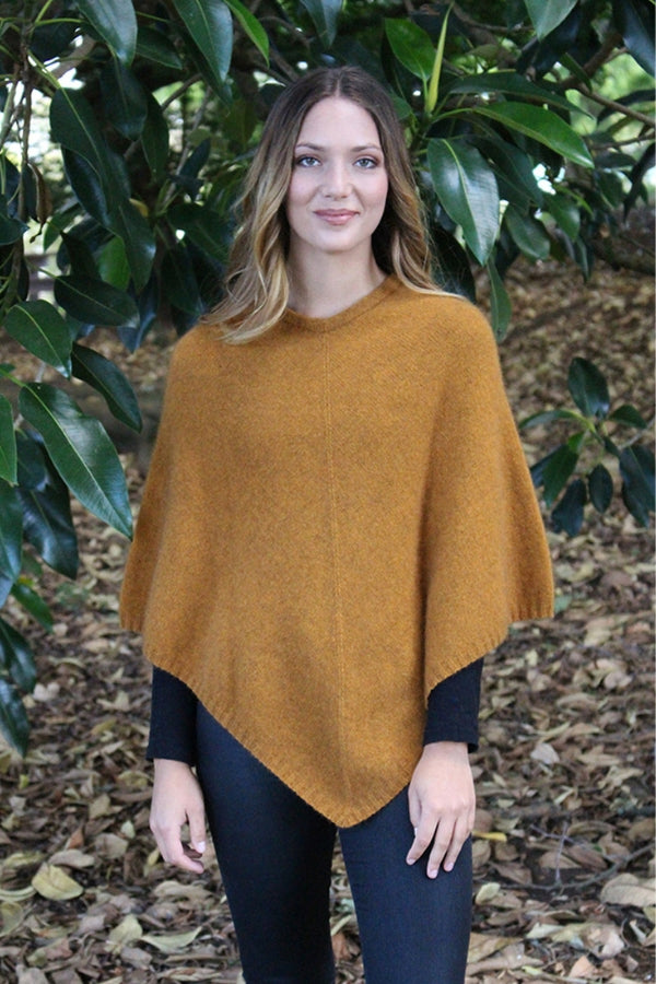 Gold possum and merino wool poncho on female model standing in garden. Warm, soft, lightweight possum and merino wool. Lothlorian
