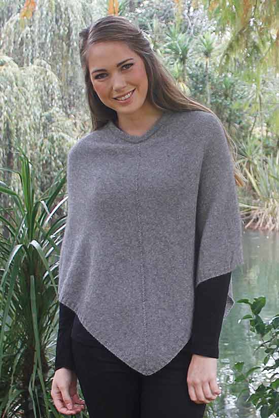 Silver grey possum and merino wool poncho on female model standing in garden. Warm, soft, lightweight possum and merino wool. Lothlorian