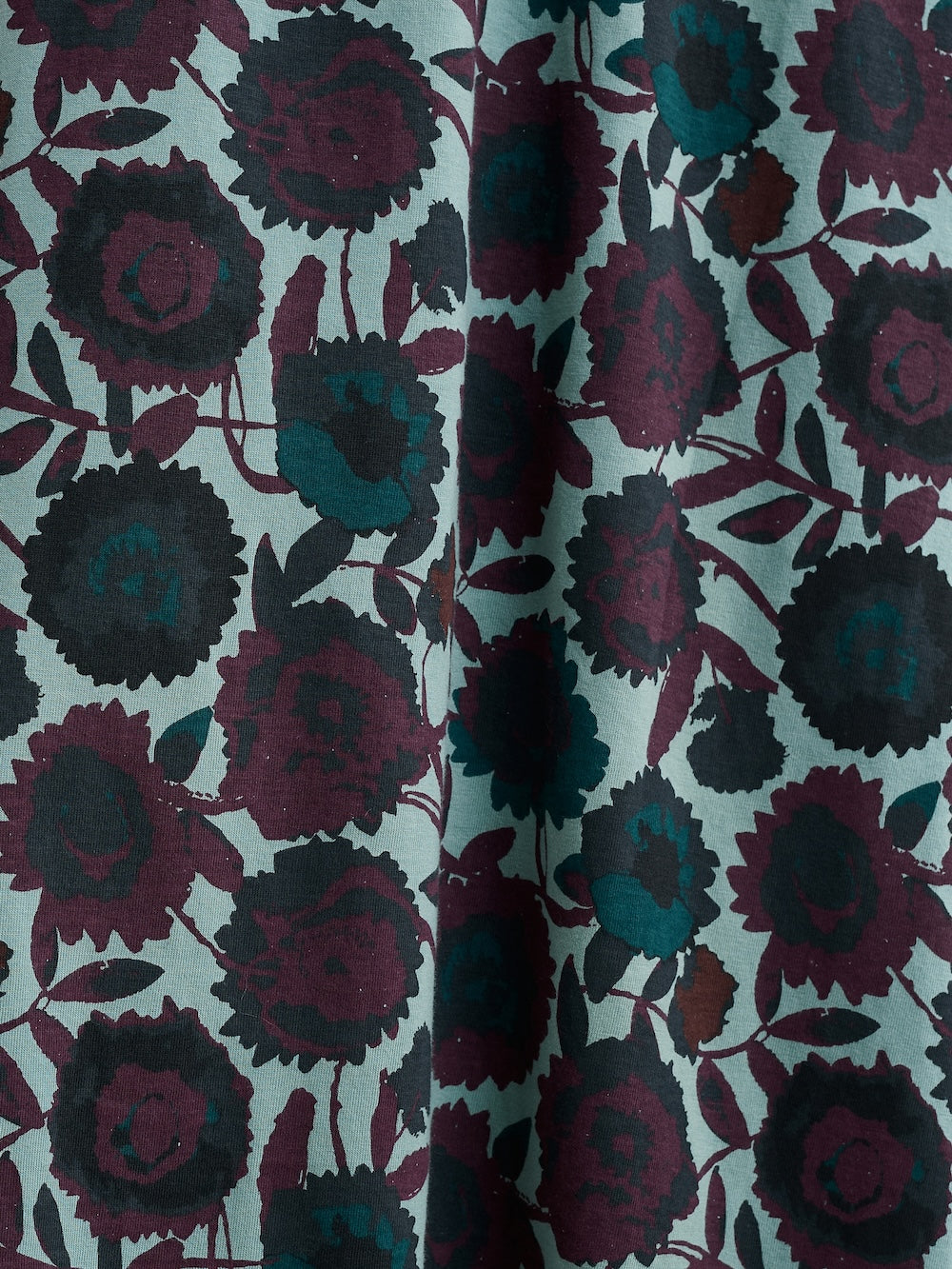 Close-up of floral patterned fabric with dark purple and black flowers on a light green background