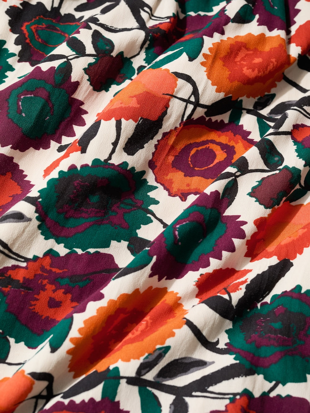Close-up of colorful floral fabric with orange, purple, and green patterns on a white background.