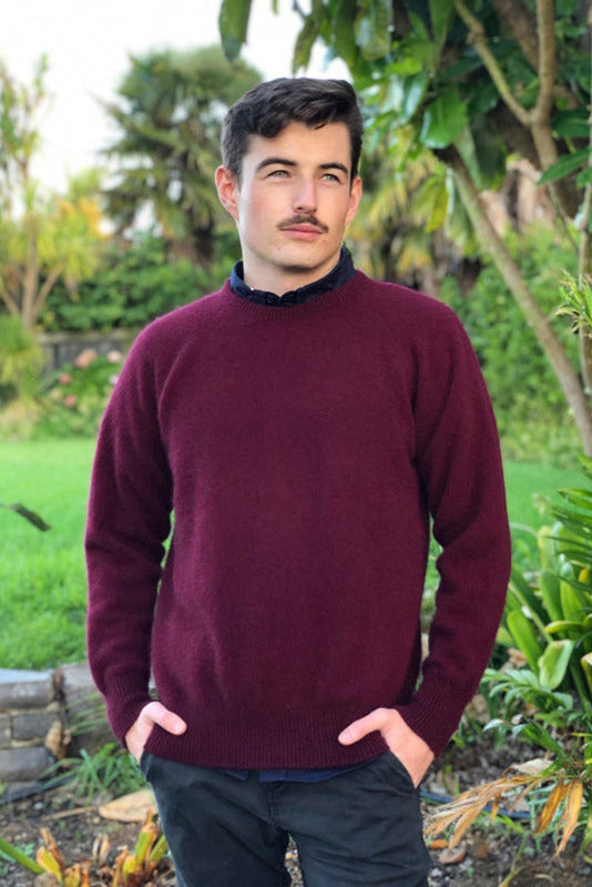 Pinot coloured men's possum merino crew neck jumper on male model standing in a garden. Super warm, comfortable and soft Lothlorian crew neck jumper for men. Soft possum fur & warm merino wool.
