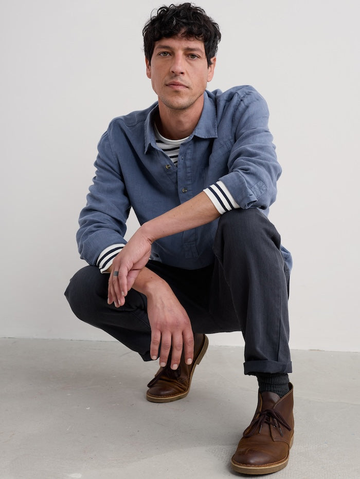 Man wearing a blue long sleeve shirt and dark pants sitting on a light grey floor.