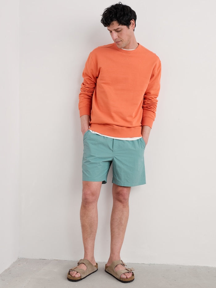 Man wearing an orange sweater and green shorts against a white background