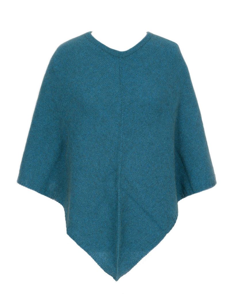 Teal blue possum and merino wool poncho on female model standing in garden. Warm, soft, lightweight possum and merino wool. Lothlorian