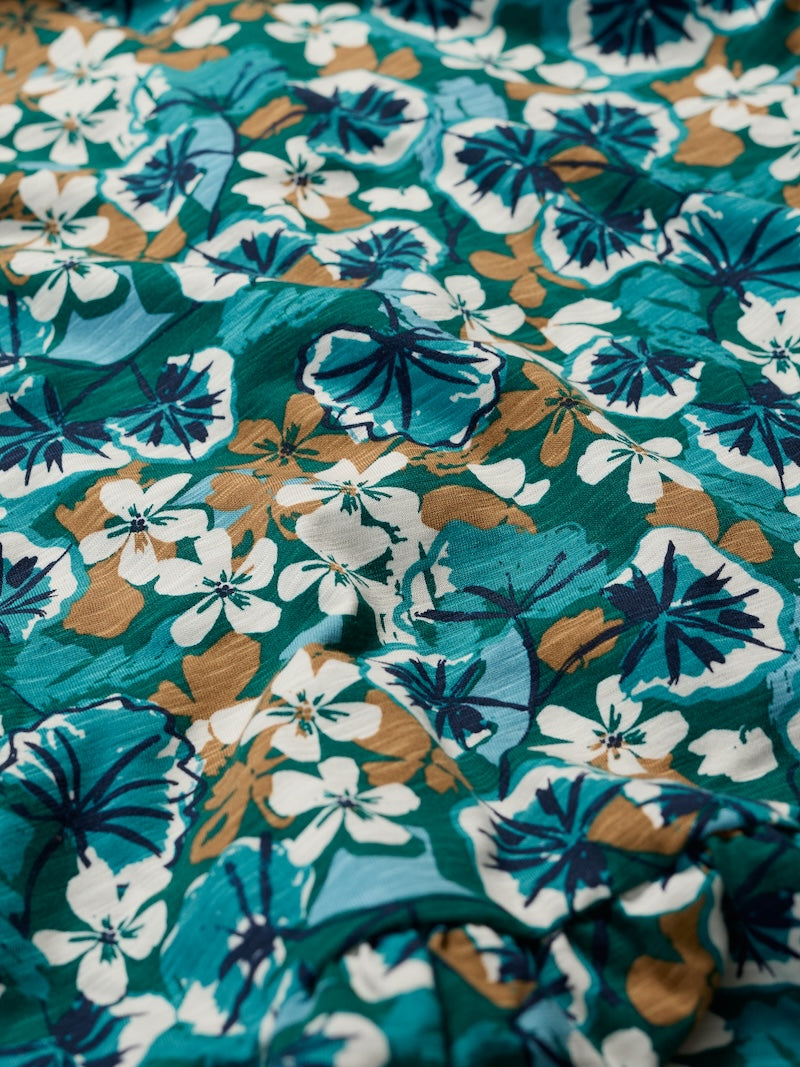 Close-up of a floral fabric with blue, brown, and white flowers on a green background.