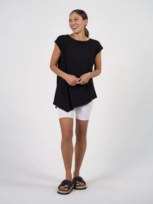 Woman wearing a black asymmetrical top and white shorts on a white background.