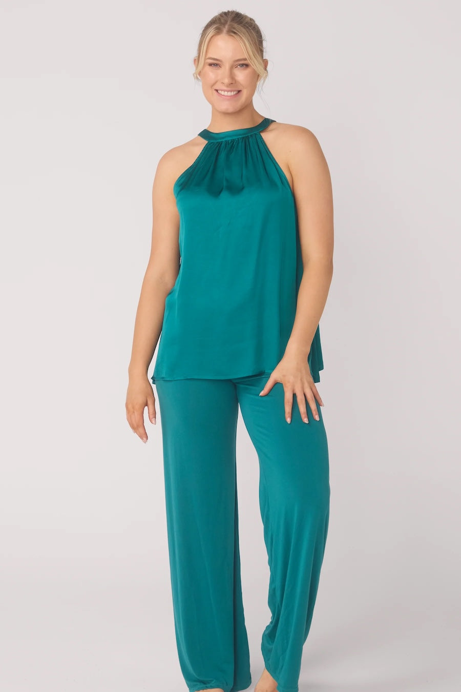 Woman wearing a teal sleeveless top and wide leg pants on a white background