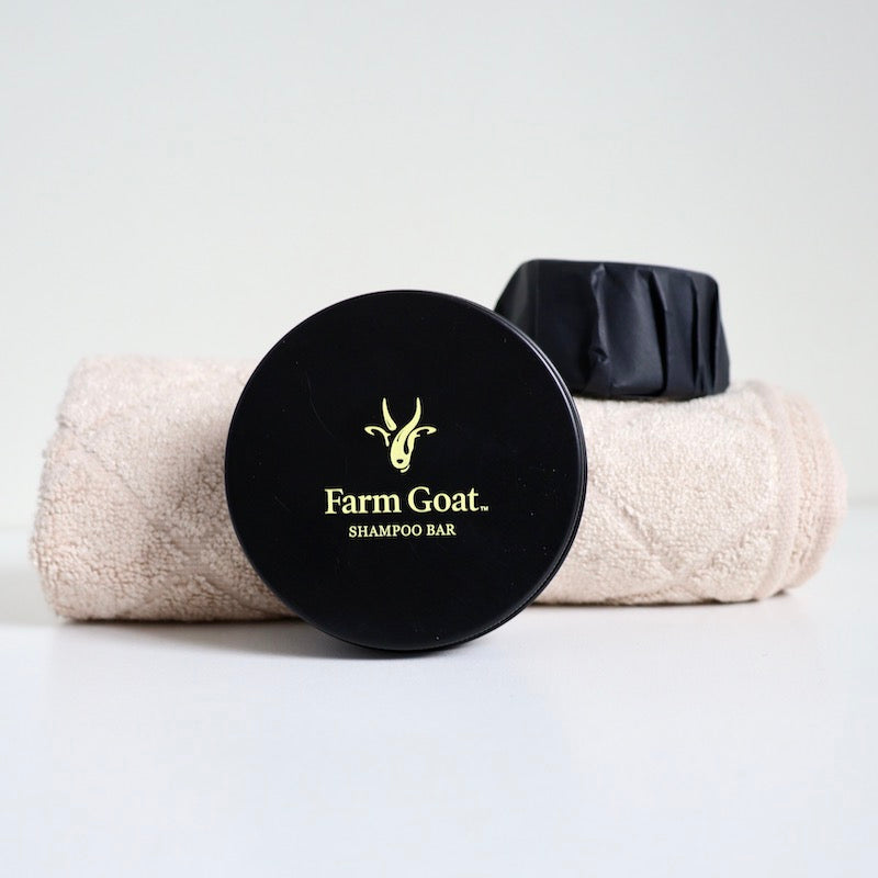 Farm Goat shampoo bar tin in front of towel with shampoo bar sitting on top of towel