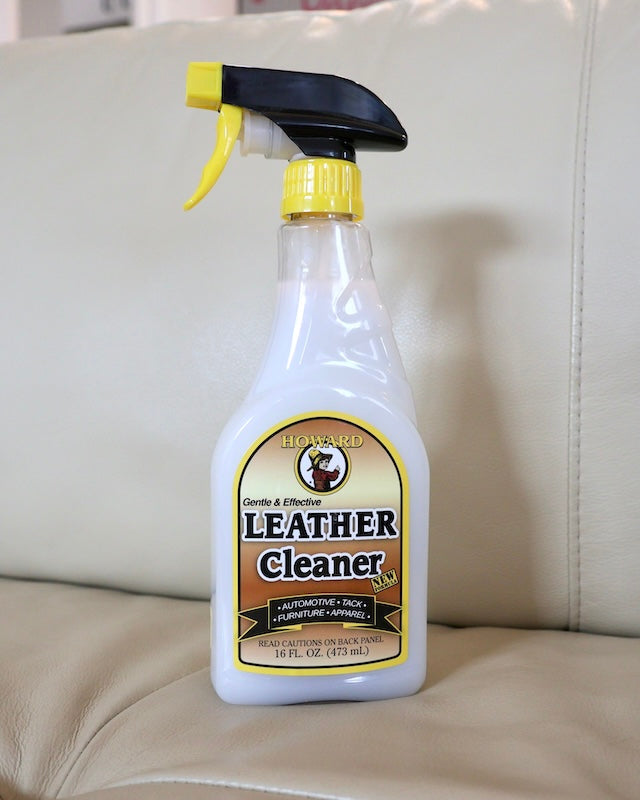 Howard leather cleaner in spray bottle sitting on leather couch. Gentle cleaner for automotive, furniture and apparel.