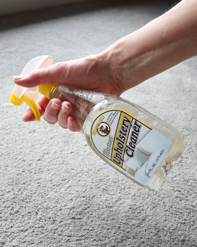 Howards upholstery cleaner spray bottle being sprayed onto grey carpet to clean. Gently breaks down stains, spills and dirt on most types of upholstery, carpets, couches, chairs, rugs, and blankets.