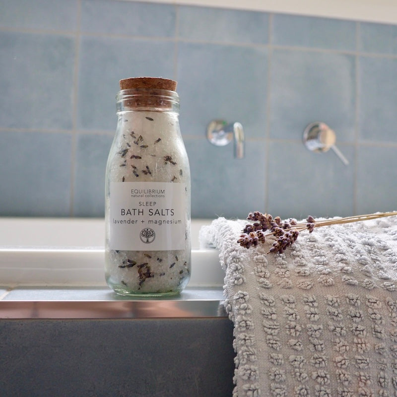 Sleep bath salts with lavender and magnesium in glass jar sitting on bath tub with towel and lavender