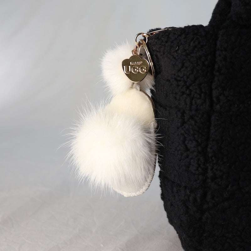 White fluffy keychain with UGG logo attached to a black textured surface.