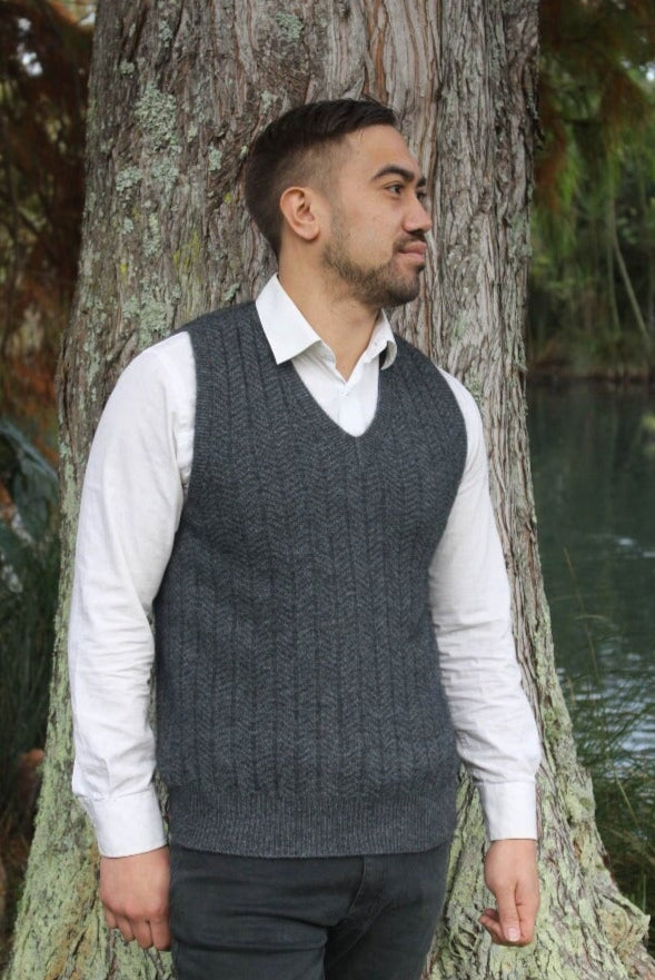 Charcoal grey possum and merino wool vest on male model standing outside among trees. Warm, wool mens vest