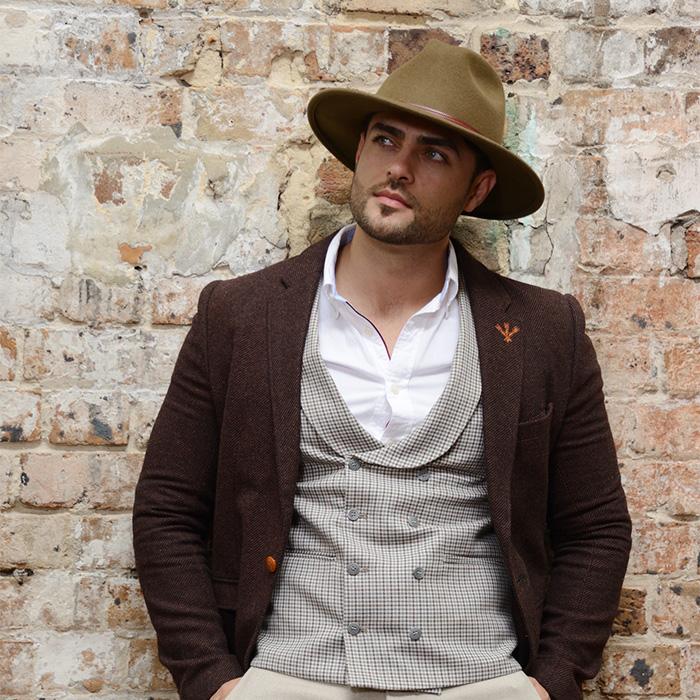 Wool felt fedora hat with brown band on male model against brick wall