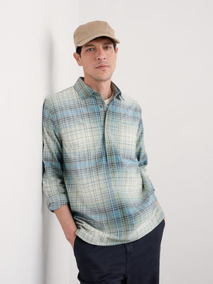 Man wearing a plaid shirt and cap against a white wall
