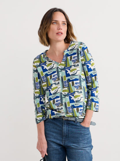 Woman wearing a patterned blouse and jeans on a plain background