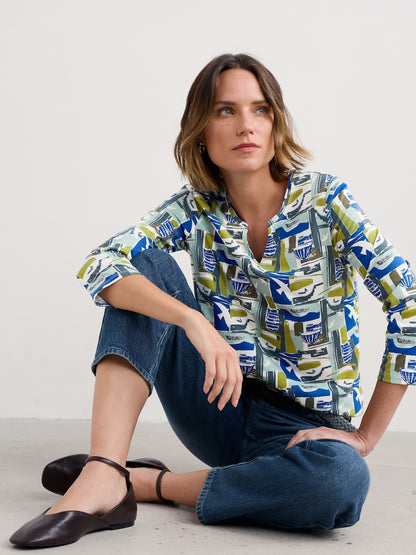 Woman wearing a patterned shirt and jeans sitting on the floor against a white background