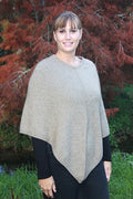 Natural possum and merino wool poncho on female model standing in garden. Warm, soft, lightweight possum and merino wool. Lothlorian