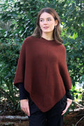 Russet brown possum and merino wool poncho on female model standing in garden. Warm, soft, lightweight possum and merino wool. Lothlorian