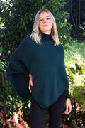 Tasman green purple possum and merino wool poncho on female model standing in garden. Warm, soft, lightweight possum and merino wool. Lothlorian