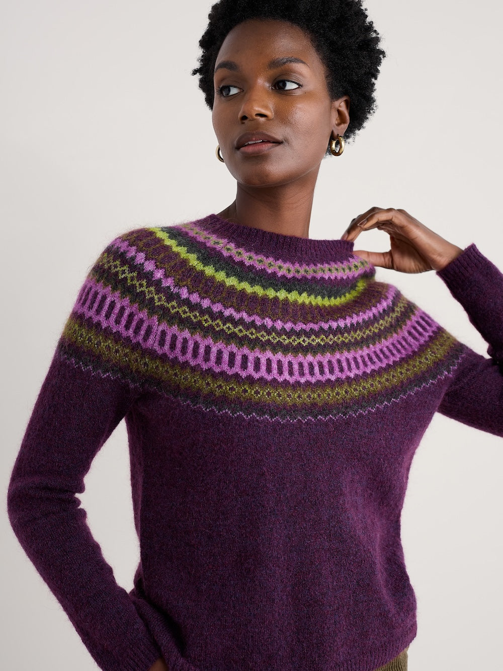 Woman wearing a purple sweater with a patterned yoke against a plain background