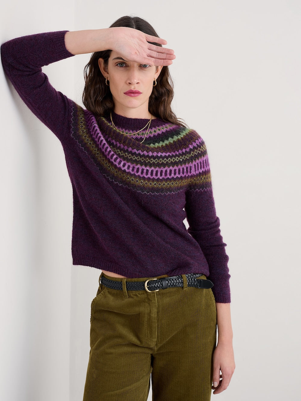 Woman wearing a purple sweater with a patterned design, standing against a plain background.