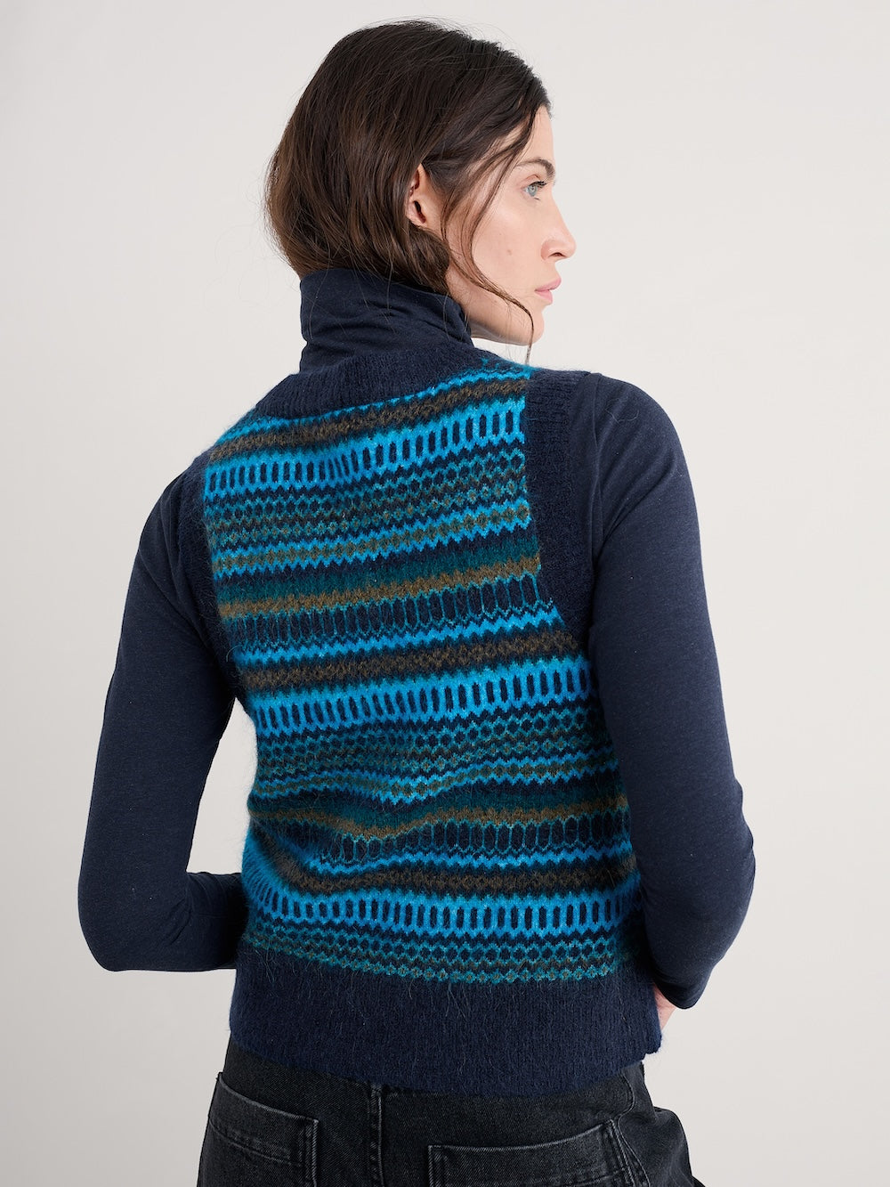 Person wearing a blue and black striped knit vest on a plain background