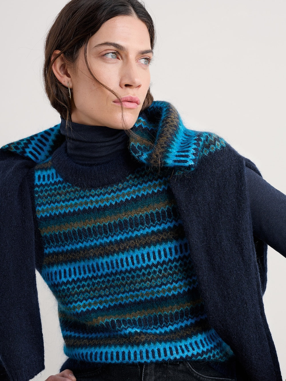 Woman wearing a blue and black striped vest with a plain background