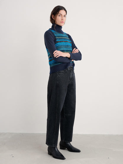 Person wearing a patterned turtleneck, vest and black pants on a plain background