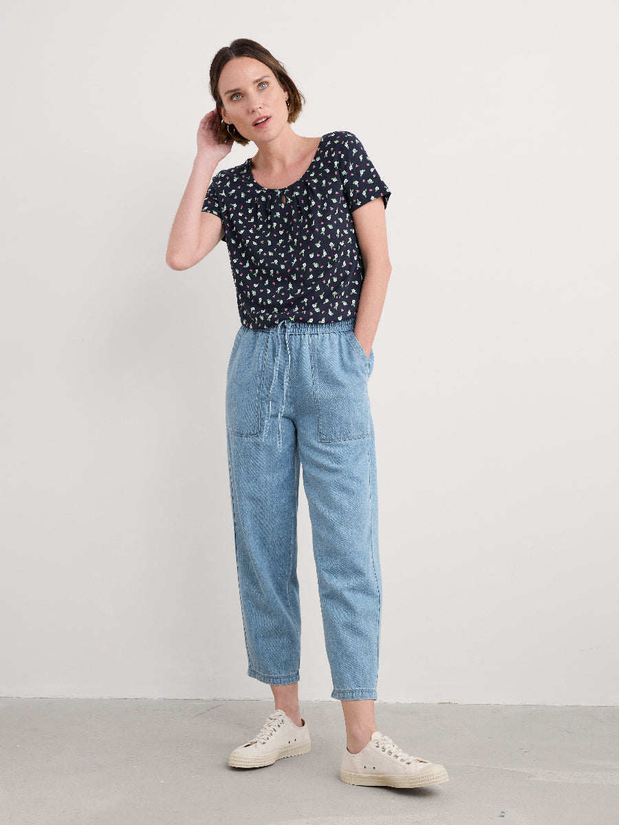 Woman wearing a black floral top and light blue jeans against a white background