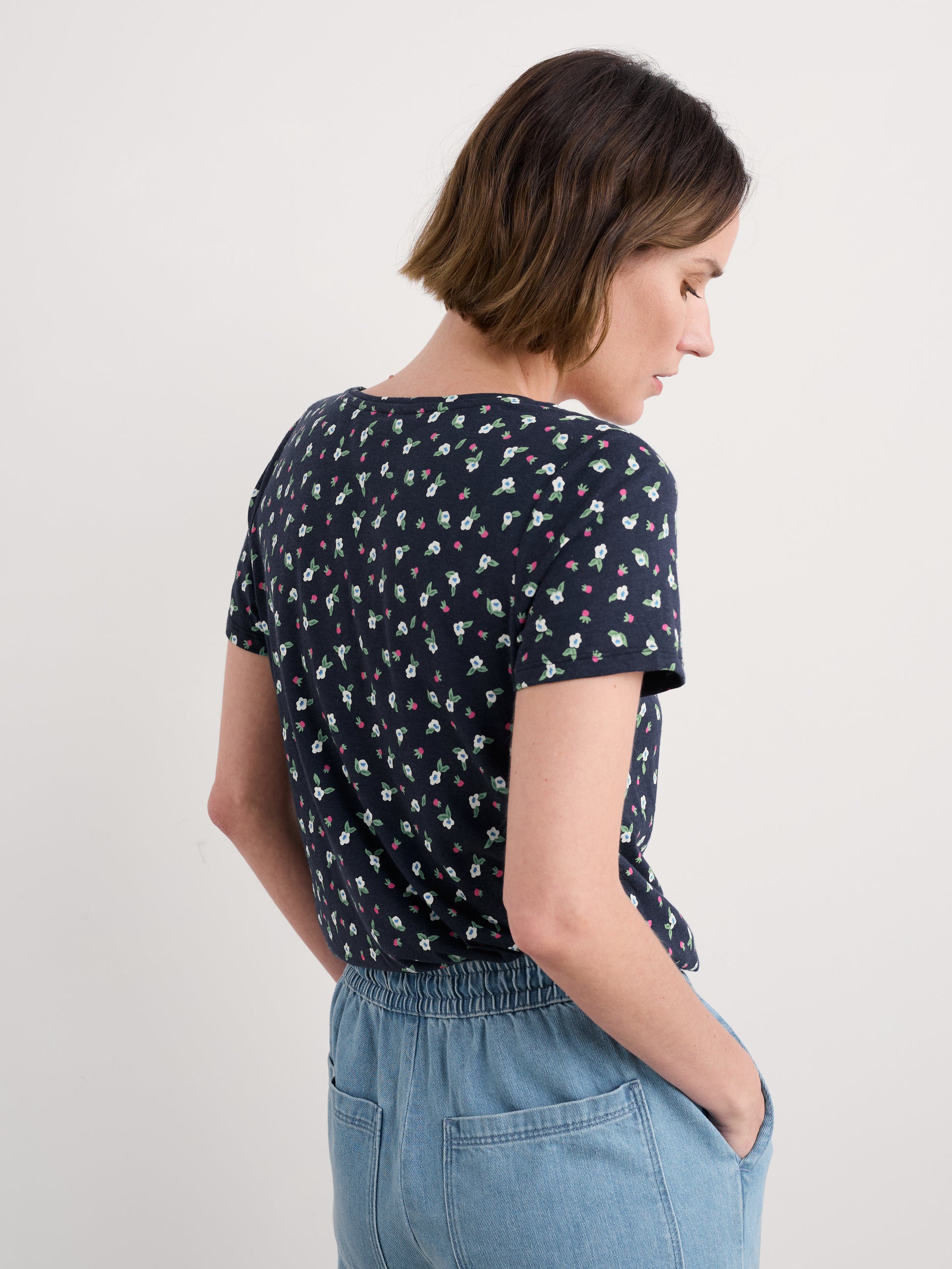 Woman wearing a navy blue floral patterned shirt and light blue jeans on a plain background