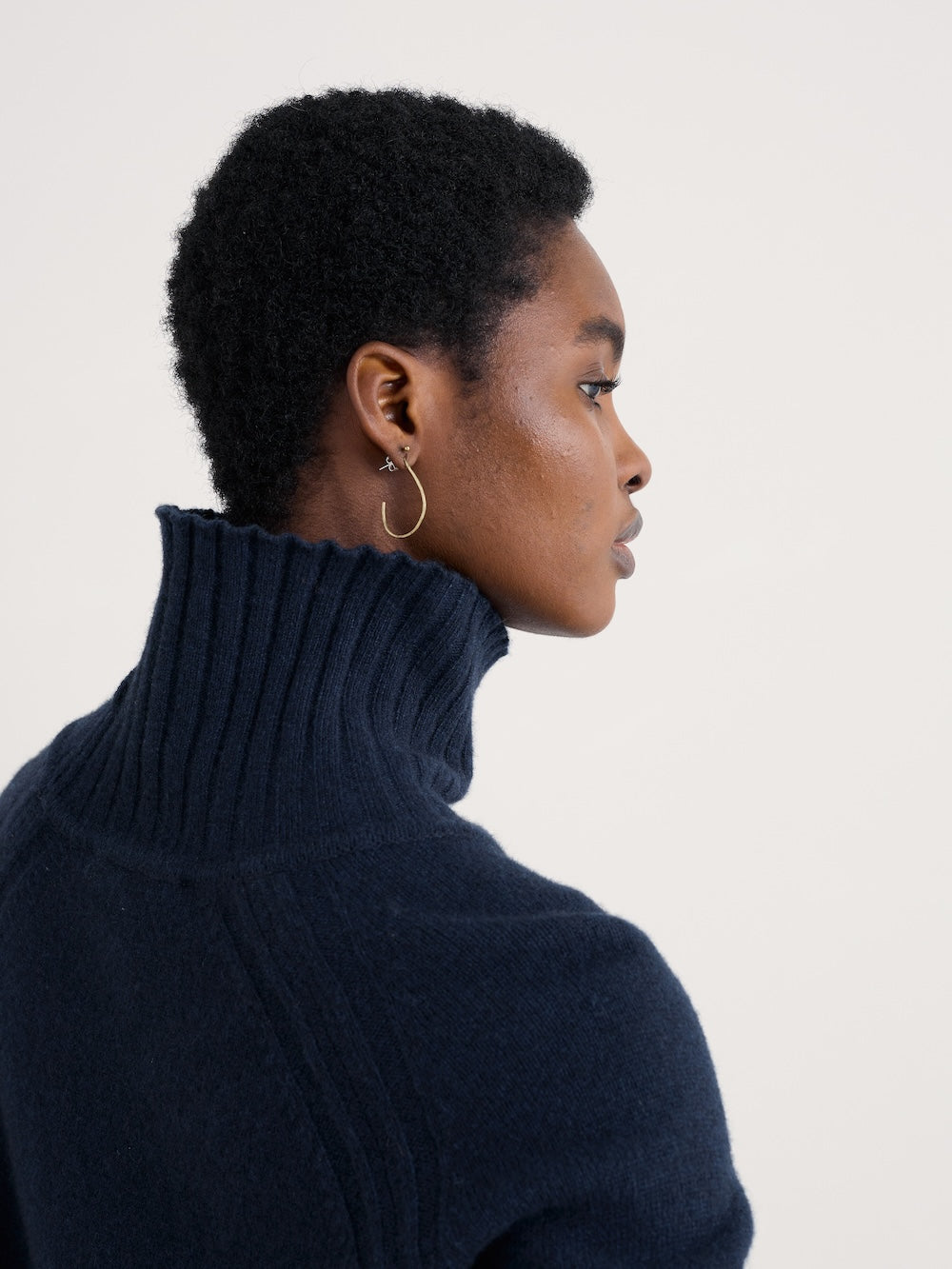 Woman wearing a dark blue turtleneck sweater against a plain background