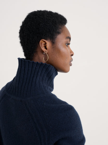 Woman wearing a dark blue turtleneck sweater against a plain background