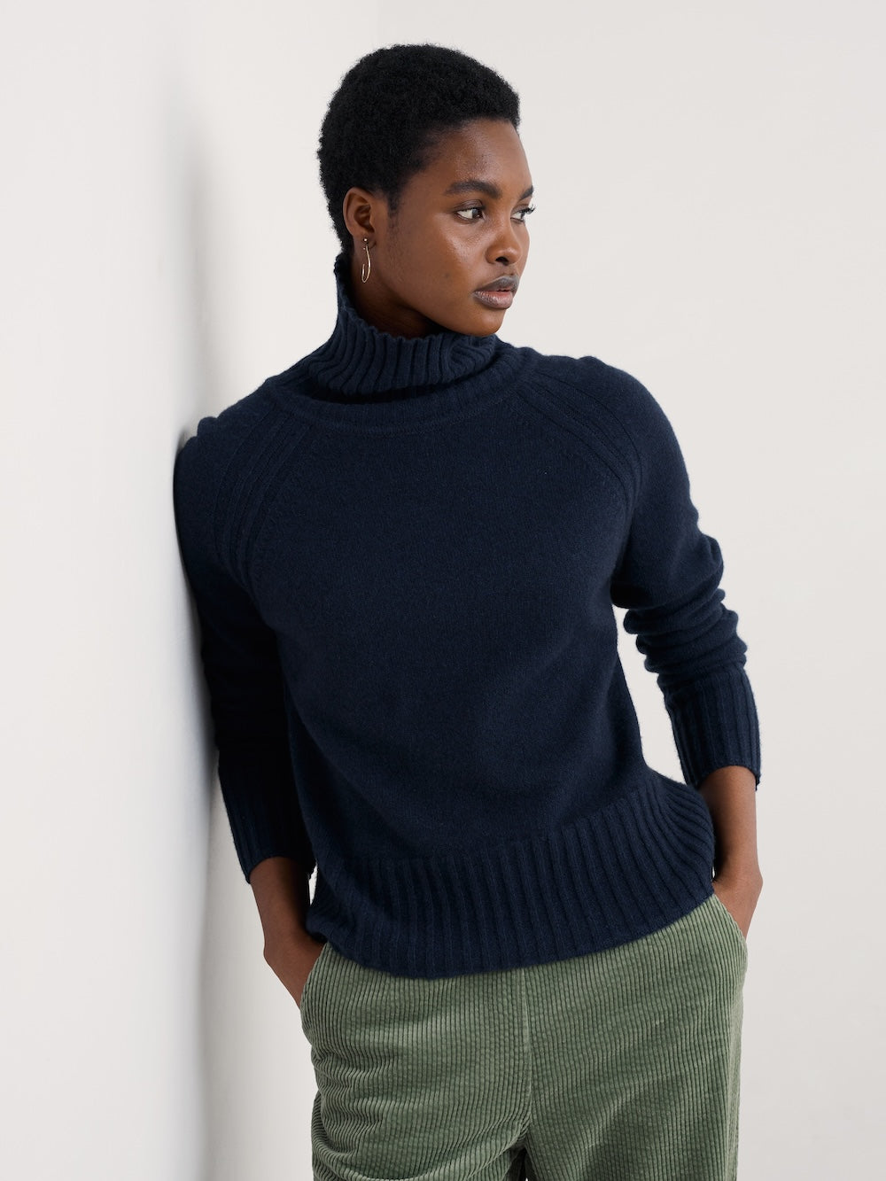 Person wearing a navy sweater and green pants against a white background