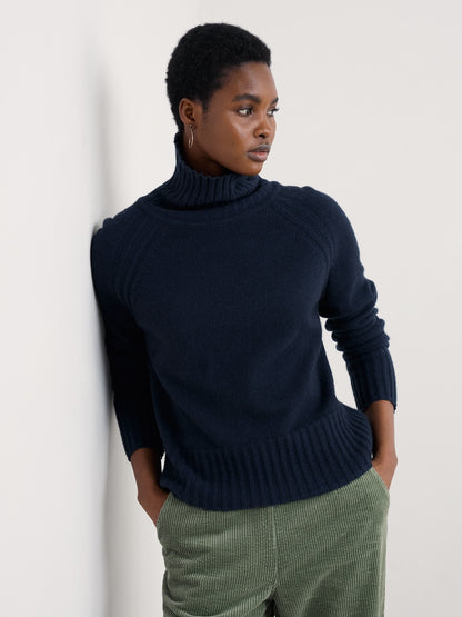 Person wearing a navy sweater and green pants against a white background