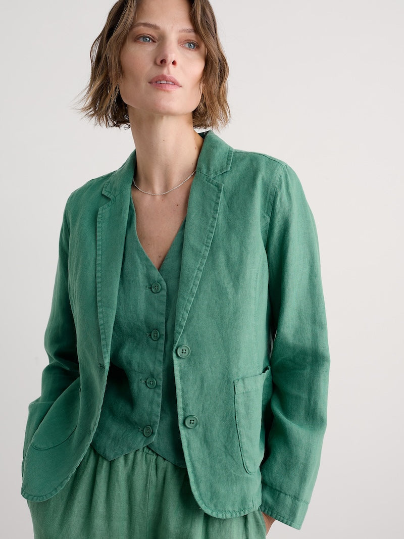 Woman wearing a green blazer over a matching top against a plain background