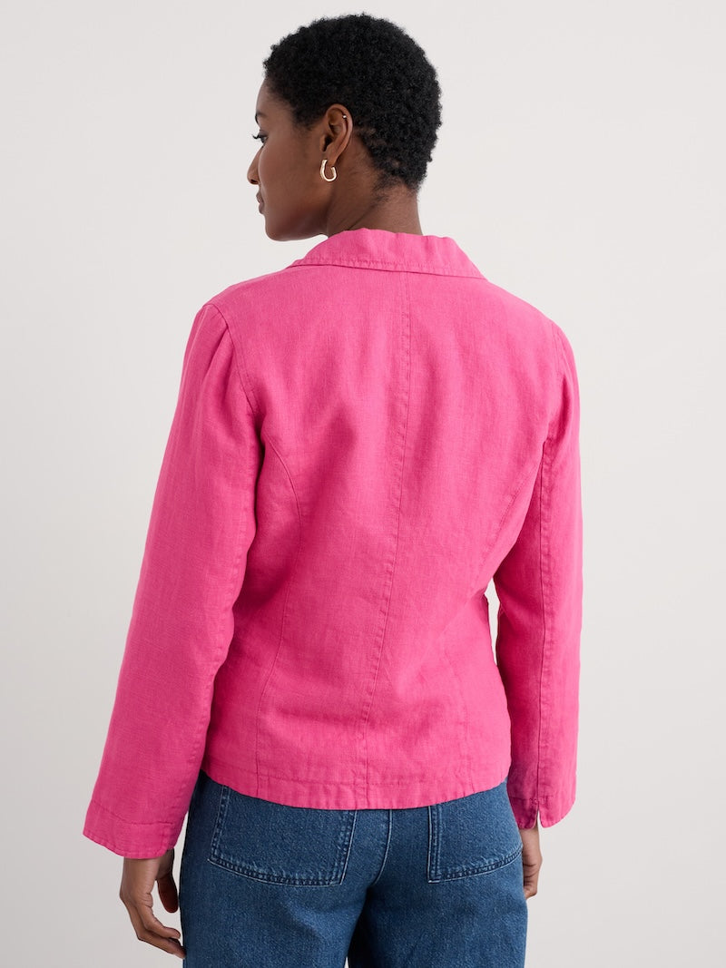 Woman wearing a pink jacket and blue jeans on a plain background