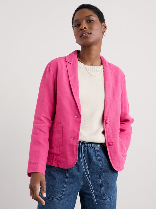 Woman wearing a bright pink blazer over a white sweater and blue jeans on a light grey background