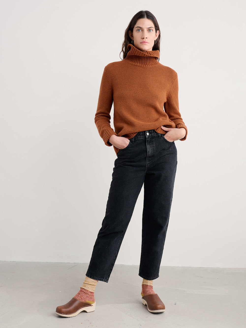 Woman wearing a brown turtleneck sweater and black jeans on a white background