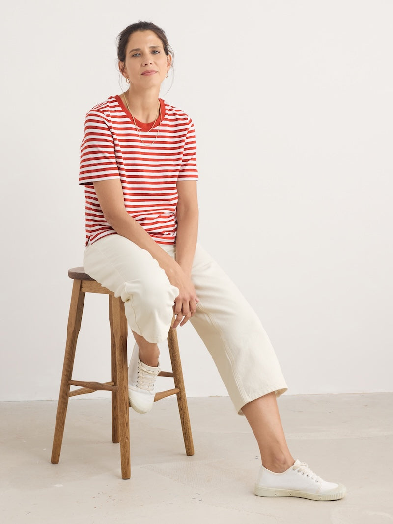 Woman sitting on a wooden stool wearing a red and white striped shirt and white pants.