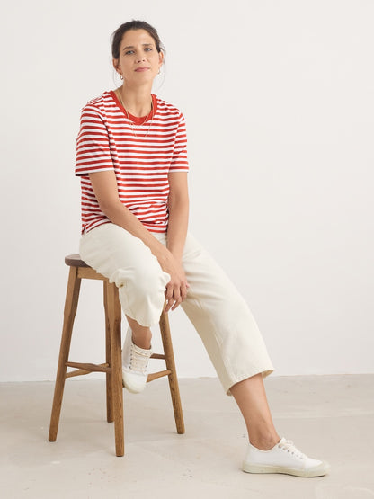 Woman sitting on a wooden stool wearing a red and white striped shirt and white pants.