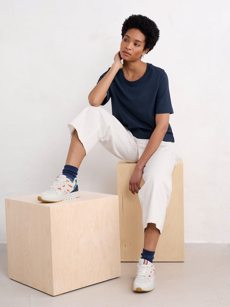 Woman sitting on a wooden block wearing a navy shirt, white pants, and colourful socks.