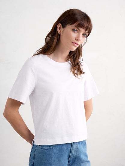 Woman wearing a white t-shirt and blue jeans against a plain background
