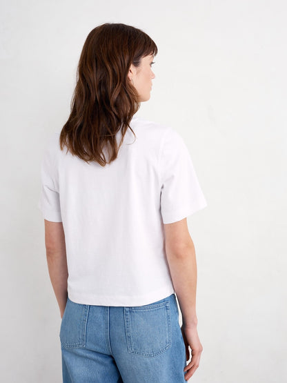 Woman wearing a white t-shirt and blue jeans against a plain background