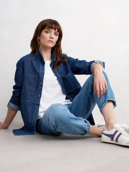Woman wearing a denim jacket and jeans sitting on the floor against a white background