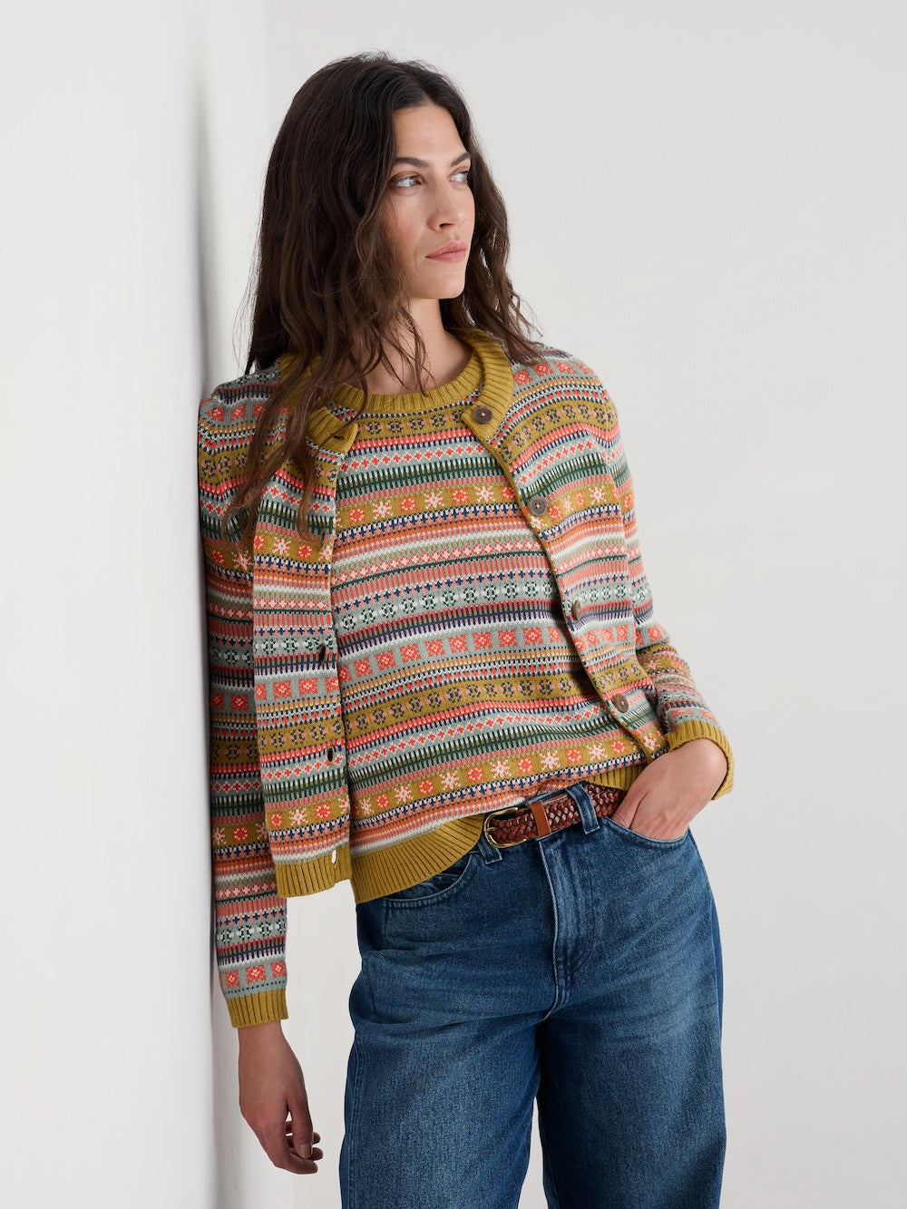 Woman wearing a colourful patterned cardigan and blue jeans against a white background