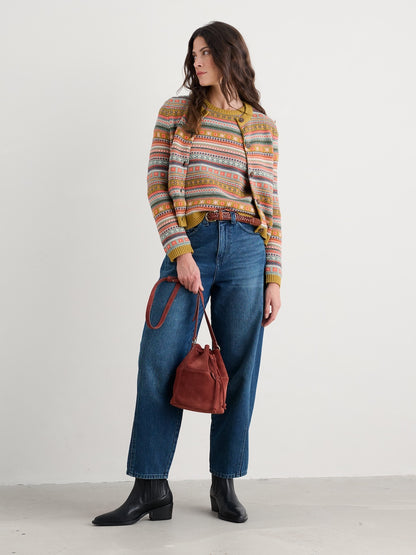 Woman wearing a patterned cardigan and blue jeans, holding a brown leather bag on a white background