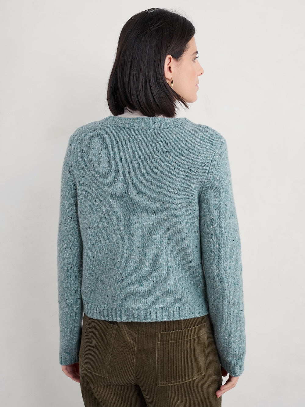Person wearing a teal knitted cardigan against a plain background